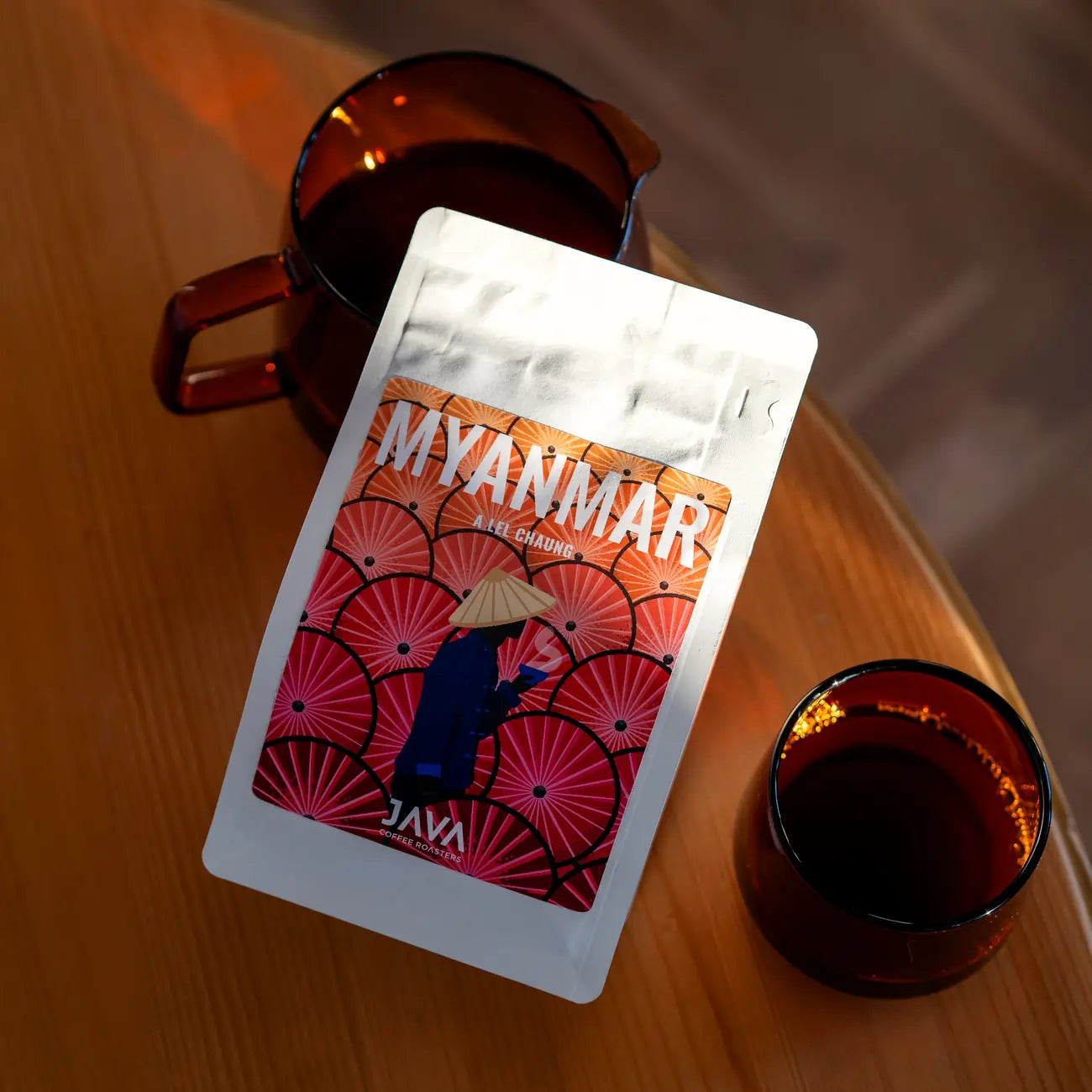 Kawa ziarnista Myanmar Ale Chaung od JAVA Coffee Roasters – opakowanie na drewnianym stole obok dzbanka i szklanki z kawą
