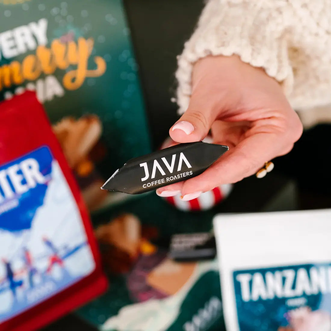 Czekoladka JAVA Coffee Roasters trzymana w dłoni na tle świątecznego zestawu kawy