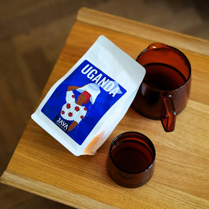 Widok z góry na kawę JAVA Coffee Roasters Uganda Rubirizi 250 g z serwerem i filiżanką na drewnianym stole – świeżo palona kawa specialty 100% Arabica.
