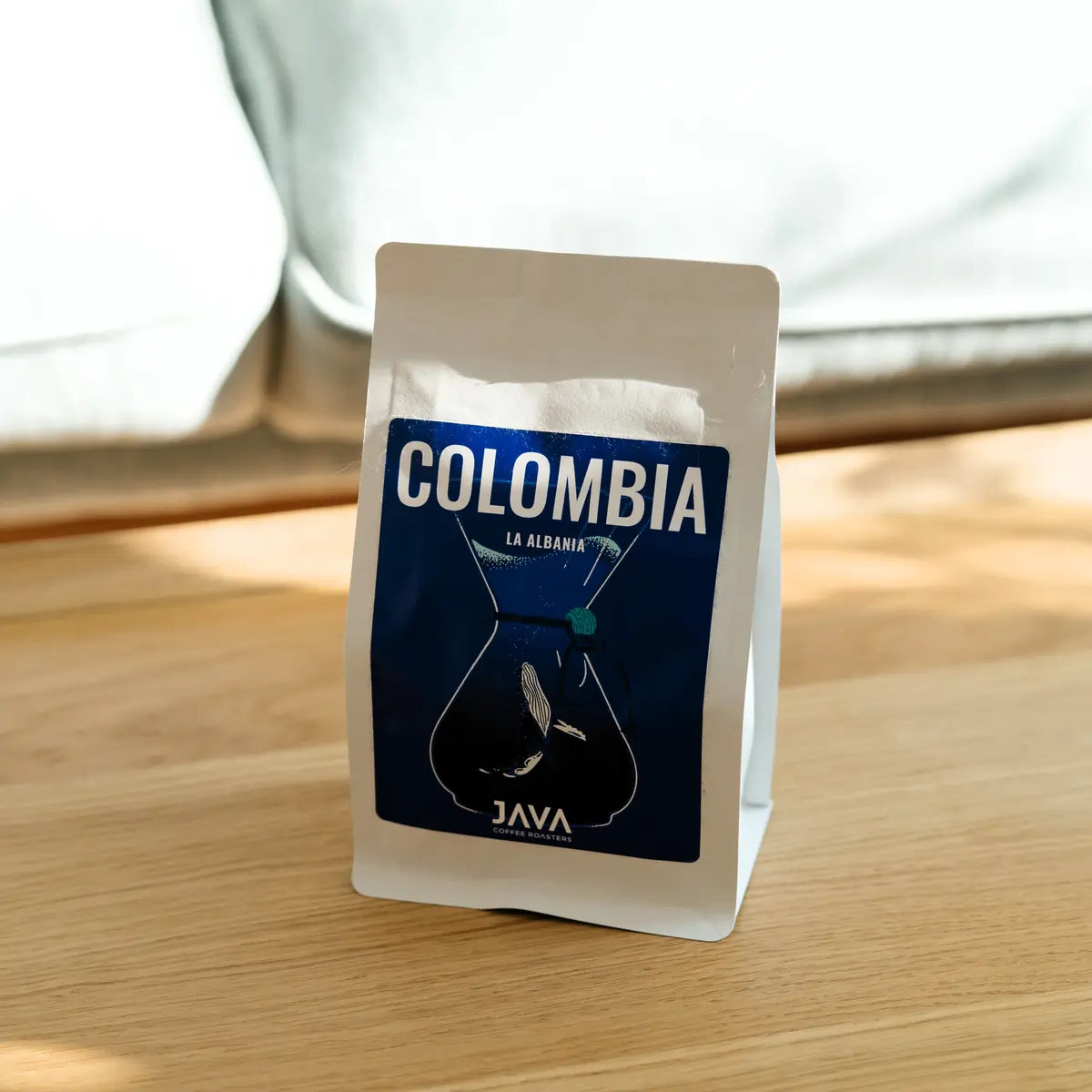 Kawa speciality Java Coffee Roasters Colombia La Albania w białym opakowaniu na drewnianym stole w naturalnym świetle
