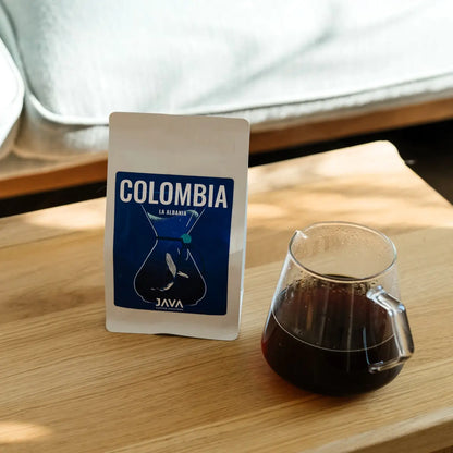 Kawa speciality Java Coffee Roasters Colombia La Albania w białym opakowaniu obok dzbanka z czarną kawą na drewnianym stole