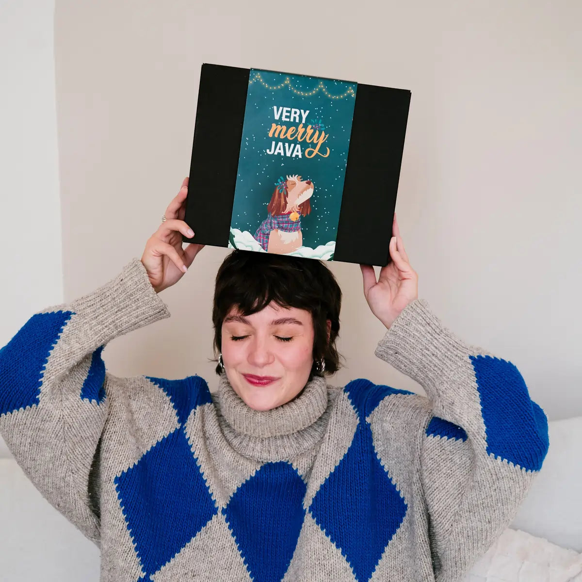 Osoba trzymająca nad głową świąteczne pudełko Very Merry Java od JAVA Coffee Roasters – lifestyle zdjęcie prezentowego zestawu kawowego.
