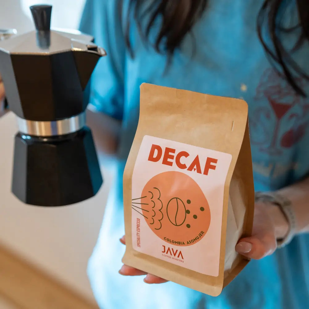 Kawa bezkofeinowa Java Coffee Roasters Decaf Colombia Asomuier 250g w brązowym opakowaniu trzymana obok kawiarki moka