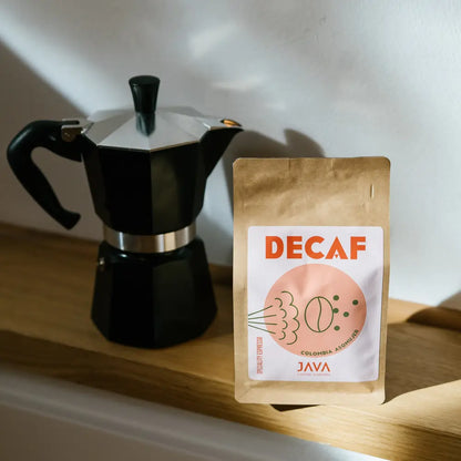 Kawa bezkofeinowa Java Coffee Roasters Decaf Colombia Asomuier 250g stojąca obok kawiarki moka na drewnianej półce w świetle słońca