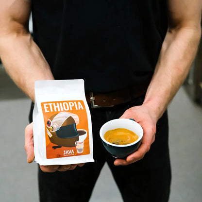 Kawa Ethiopia Gatta od JAVA Coffee Roasters – barista trzyma opakowanie kawy specialty i filiżankę espresso, zdjęcie lifestyle w palarni