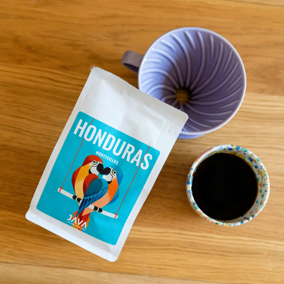 Kawa Java Honduras Montecillos 250g w białym opakowaniu obok drippera i filiżanki z kawą, ujęcie z góry na drewnianym stole