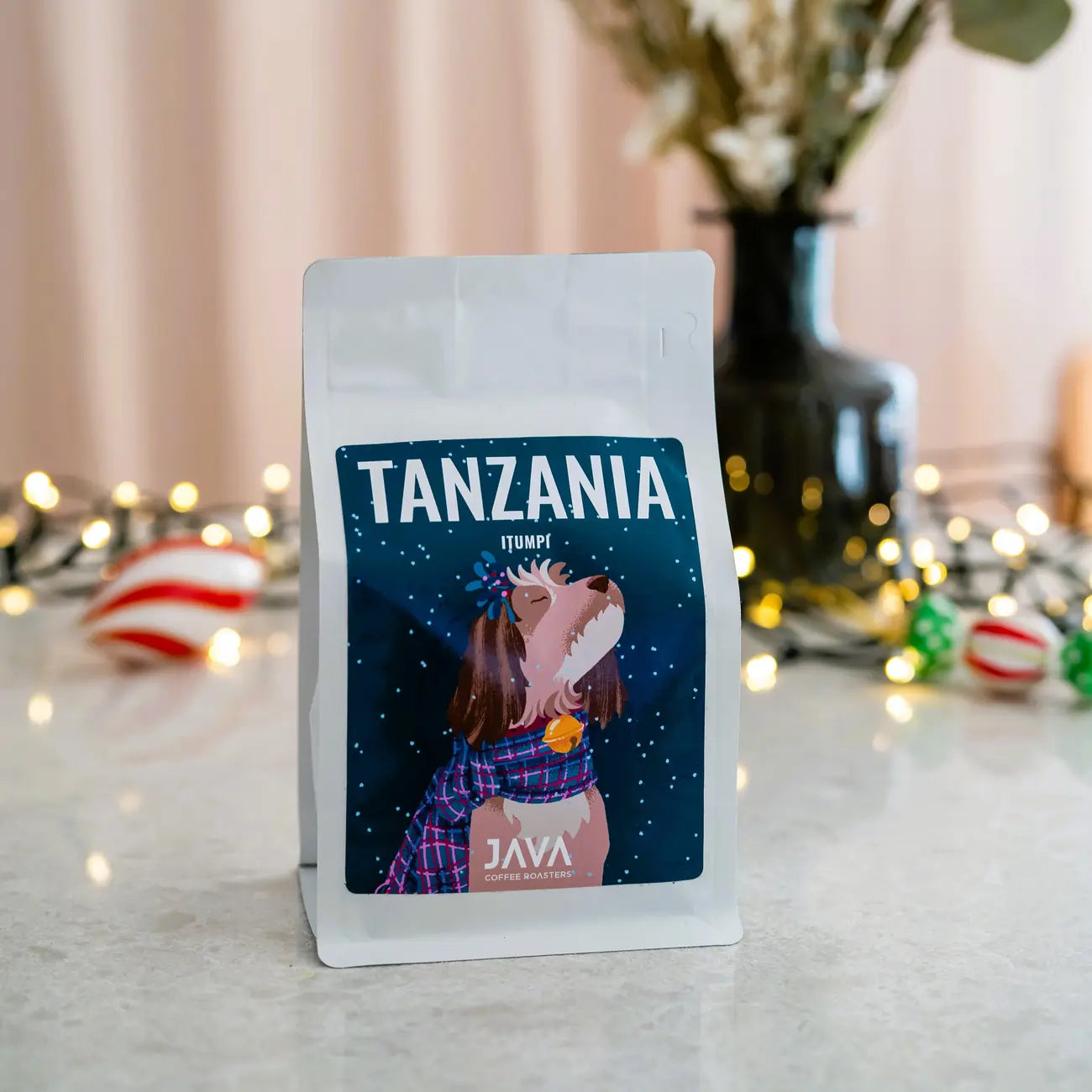 Packshot kawy JAVA Coffee Tanzania Itumpi ustawiony na blacie w świątecznej aranżacji z lampkami i dekoracjami.