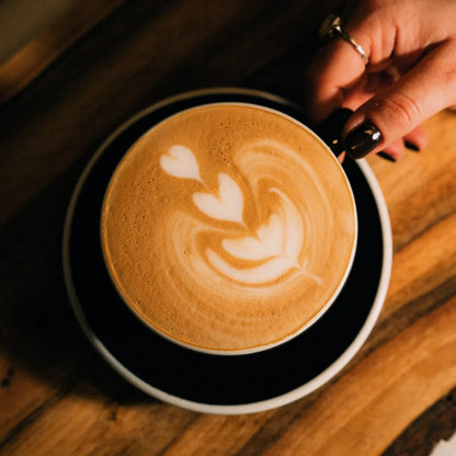 Cappuccino z wzorem latte art w kształcie rozety podawane w filiżance – zbliżenie na aksamitną mikropiankę i precyzyjny wzór mleczny.