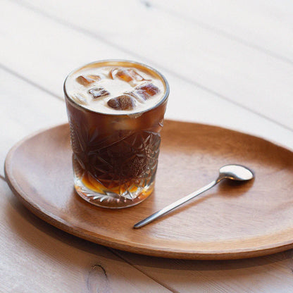 Szklanka mrożonej kawy z mlekiem i lodem na drewnianej tacy z łyżeczką – minimalistyczne ujęcie napoju.