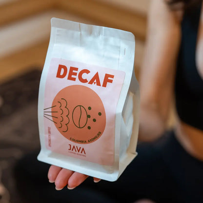 Kawa bezkofeinowa Java Coffee Roasters Decaf Colombia Asomuier 250g trzymana w dłoni, ujęcie lifestyle w ciepłym świetle