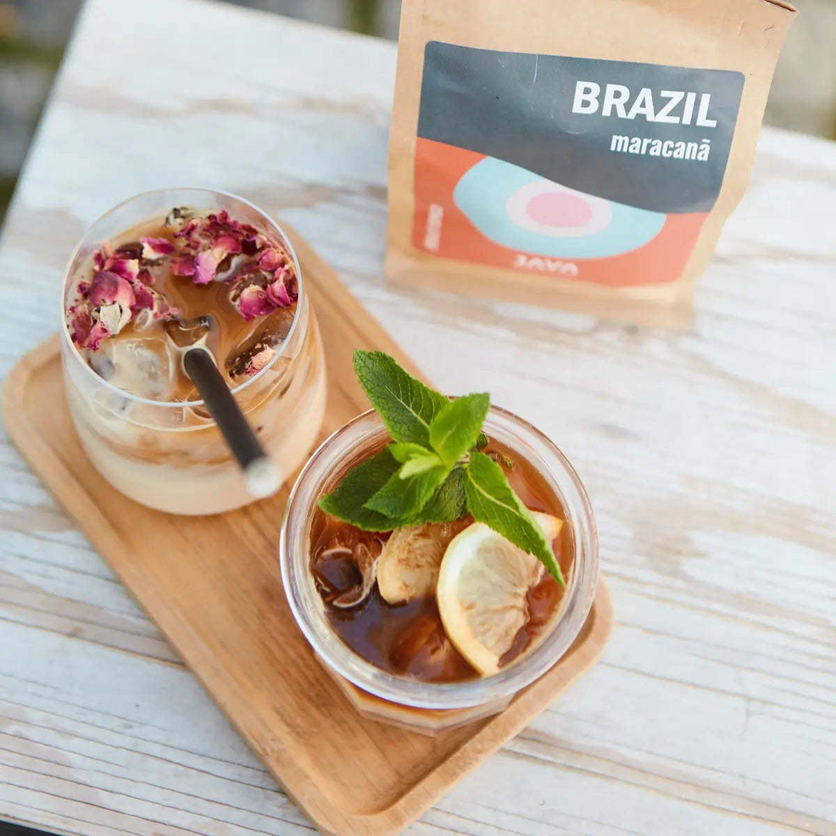 Kawa Java Coffee Roasters Brazil Maracanã w tle, dwa napoje na lodzie z miętą, cytryną i płatkami róż na drewnianej tacy.