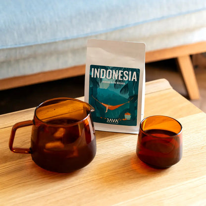 Opakowanie kawy Indonesia Ribang Gayo Musara od JAVA Coffee Roasters na stole, obok bursztynowych szklanek z zaparzoną kawą.