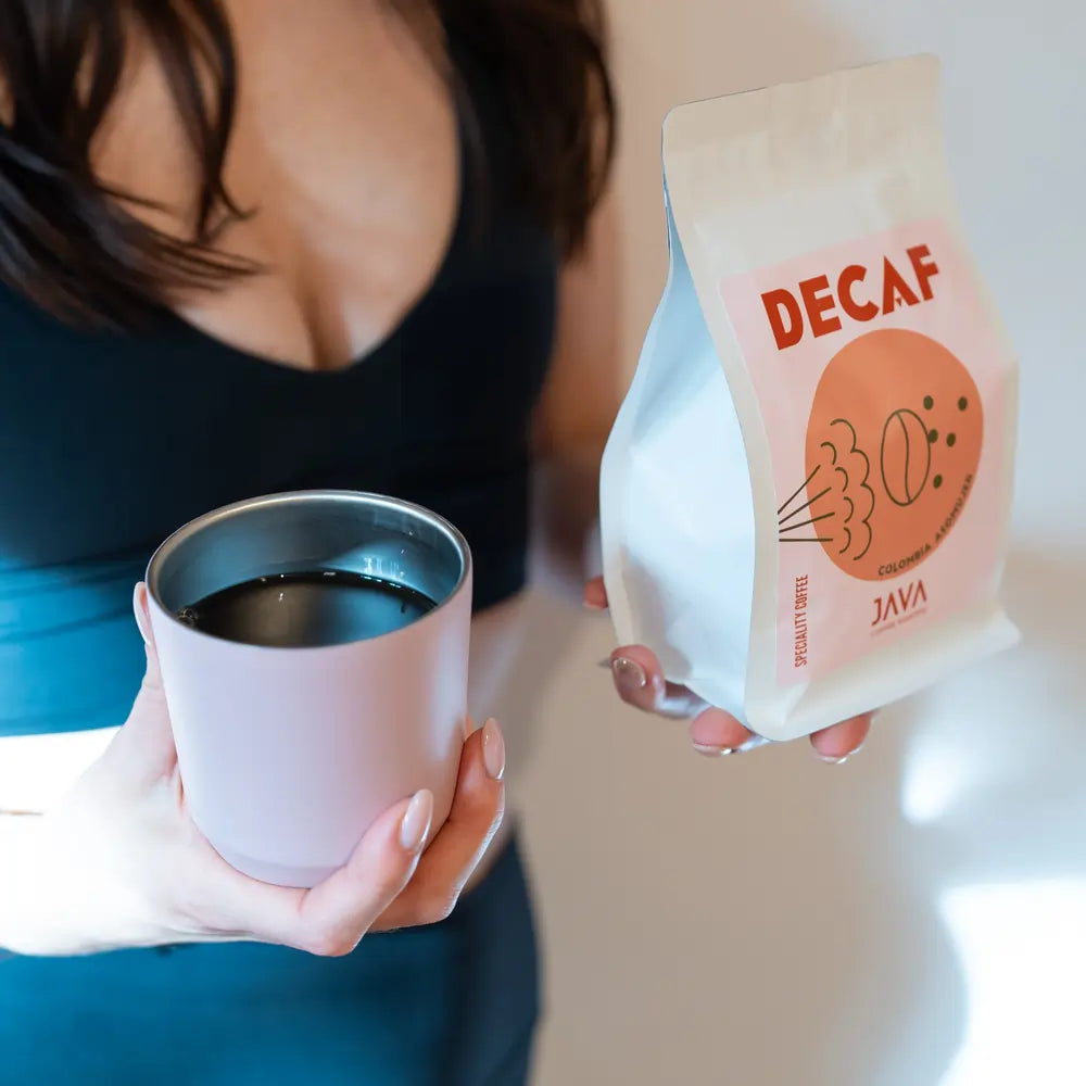 Kawa bezkofeinowa Java Coffee Roasters Decaf Colombia Asomuier 250g trzymana obok różowego kubka z kawą, ujęcie lifestyle