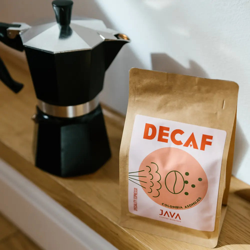Kawa bezkofeinowa Java Coffee Roasters Decaf Colombia Asomuier 250g w brązowym opakowaniu stojąca obok kawiarki moka na drewnianej półce
