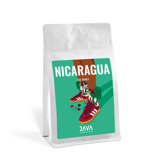 Opakowanie kawy JAVA Coffee Roasters – Nicaragua Las Nubes. Biała torebka z kolorową etykietą przedstawiającą ilustrację nóg w czerwonych sportowych butach i skarpetach ozdobionych motywem kawowych owoców i liści. Na etykiecie duży, biały napis 'NICARAGUA LAS NUBES' na zielonym tle.