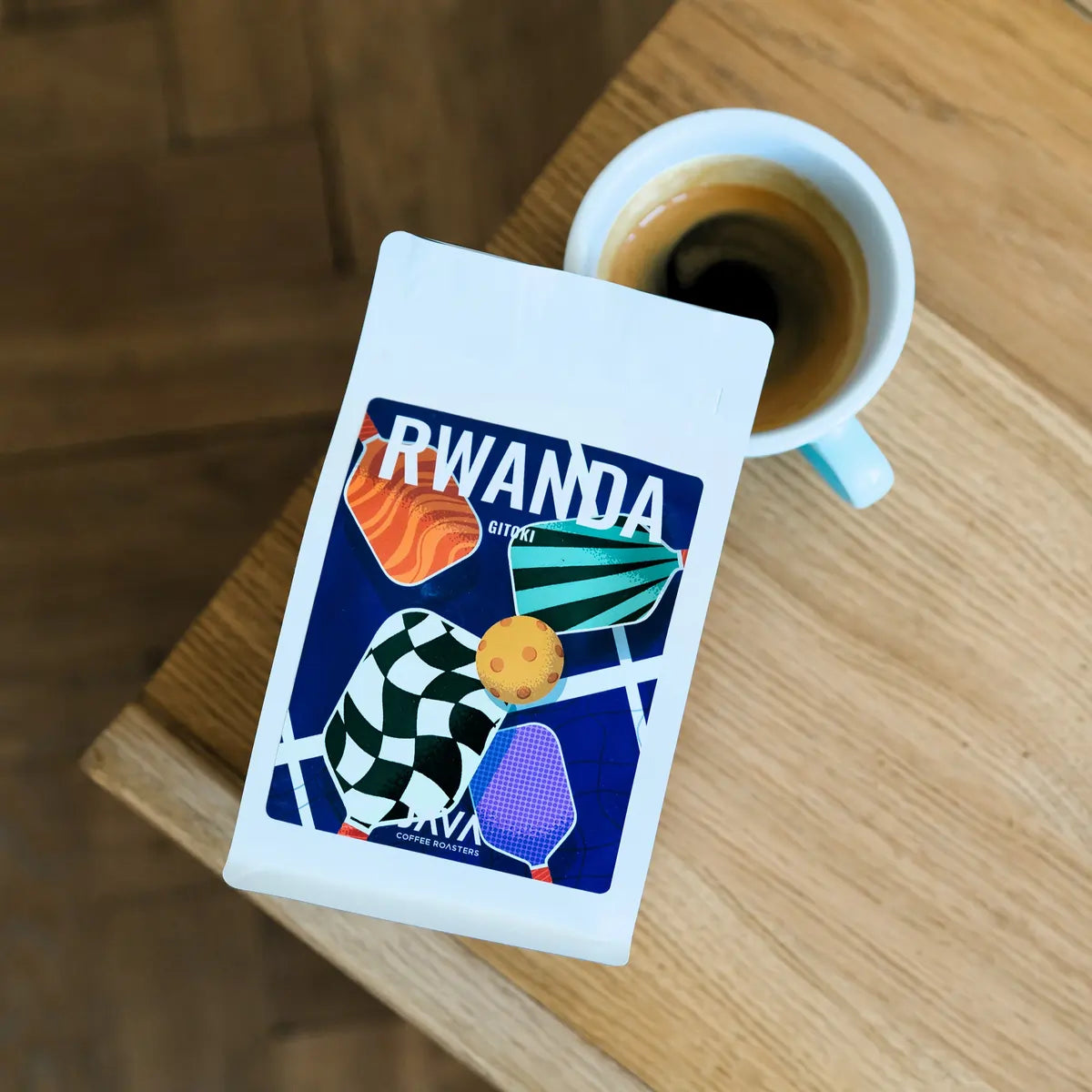 Kawa specialty Rwanda Gitoki JAVA Coffee Roasters z filiżanką espresso na drewnianym stole – ujęcie z góry