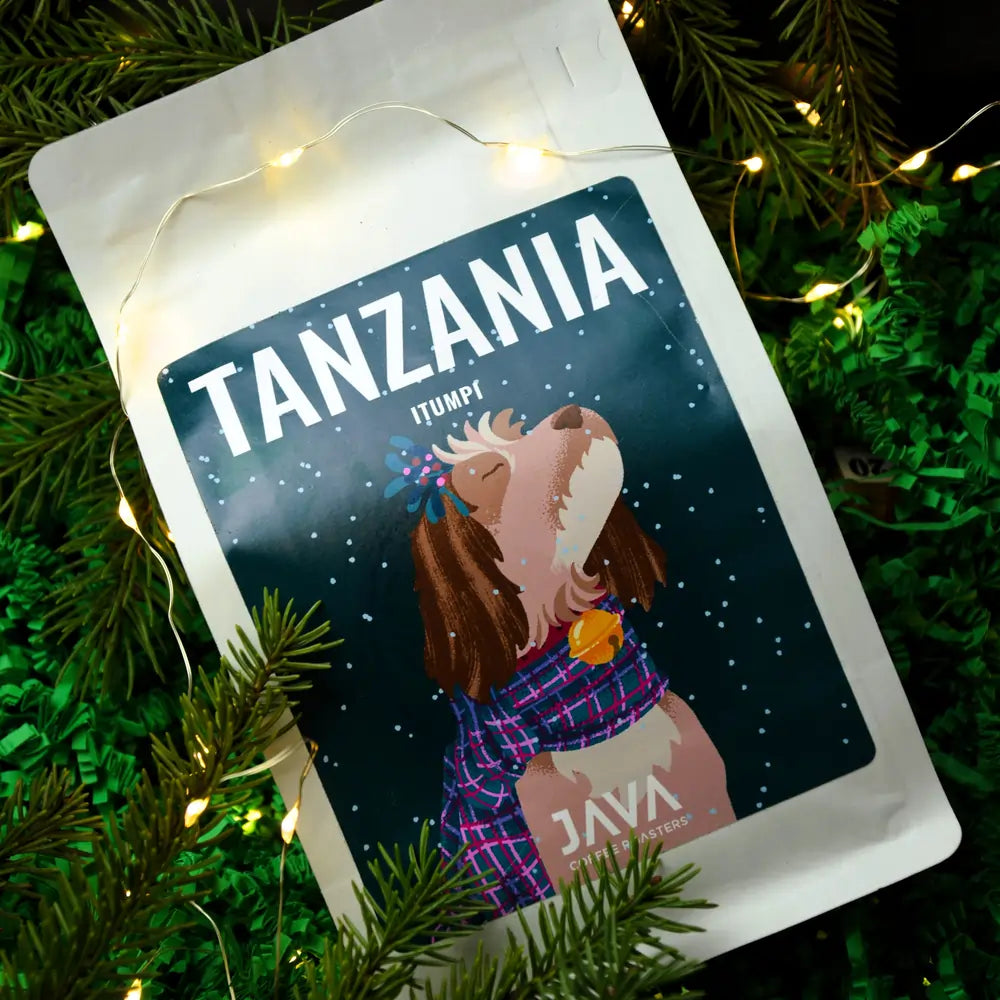Kawa Tanzania Itumpi od JAVA Coffee – świąteczne zdjęcie z zielonym igliwiem i ciepłymi lampkami, zbliżenie na opakowanie 250 g.