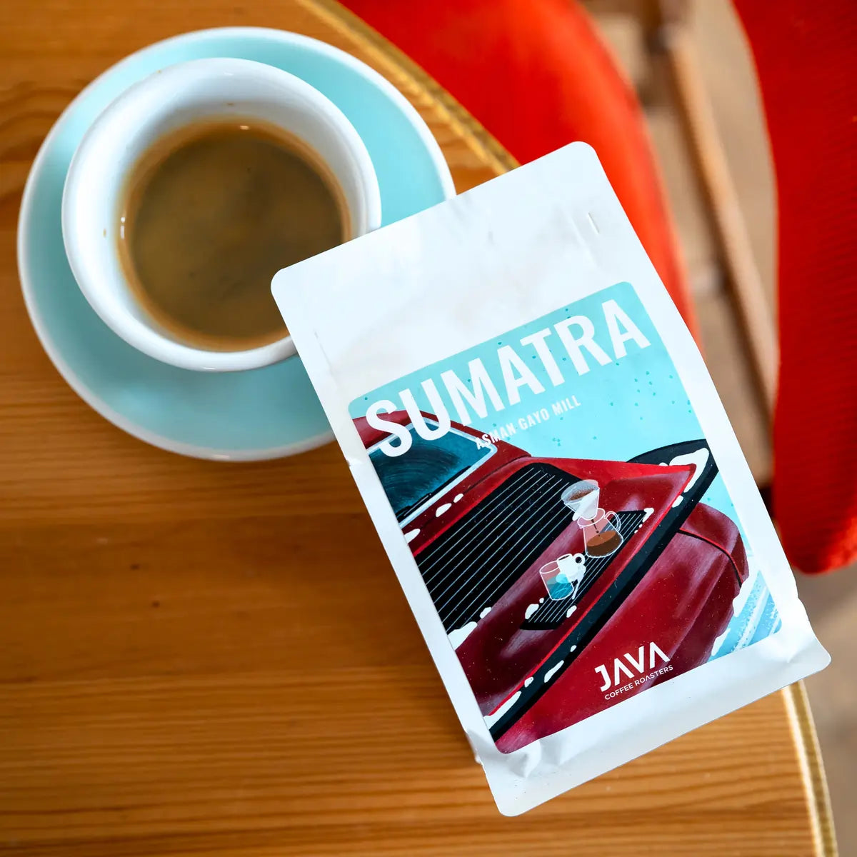 Kawa specialty Sumatra Asman Gayo Mill od JAVA Coffee Roasters – opakowanie kawy i filiżanka espresso, ujęcie z góry na drewnianym stoliku
