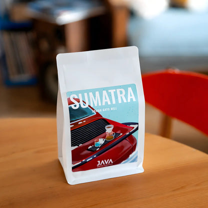 Kawa specialty Sumatra Asman Gayo Mill od JAVA Coffee Roasters – opakowanie kawy na drewnianym stoliku w kawiarni, ujęcie lifestyle