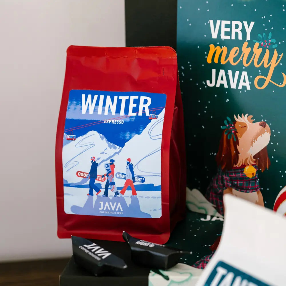 Zbliżenie na opakowanie kawy Winter Espresso Guatemala San Pedro La Laguna od JAVA Coffee, ustawione przy świątecznym pudełku z grafiką Very Merry Java