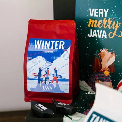 Zbliżenie na opakowanie kawy Winter Espresso Guatemala San Pedro La Laguna od JAVA Coffee, ustawione przy świątecznym pudełku z grafiką Very Merry Java