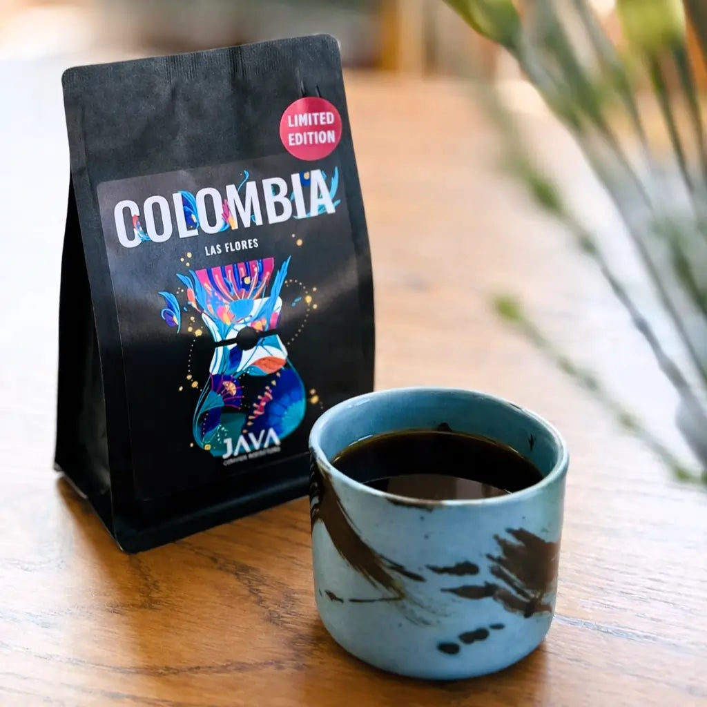 Kawa ziarnista Colombia Las Flores JAVA Coffee oraz filiżanka czarnej kawy w ujęciu lifestyle na drewnianym stole