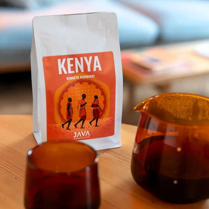 Kawa ziarnista Kenya Rungeto Karimikui JAVA Coffee Roasters na stole obok dzbanka i filiżanki z zaparzoną kawą, zdjęcie lifestyle