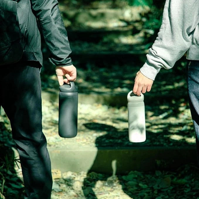 Dwie osoby trzymają termosy Kinto Day Off Tumbler podczas leśnej wycieczki