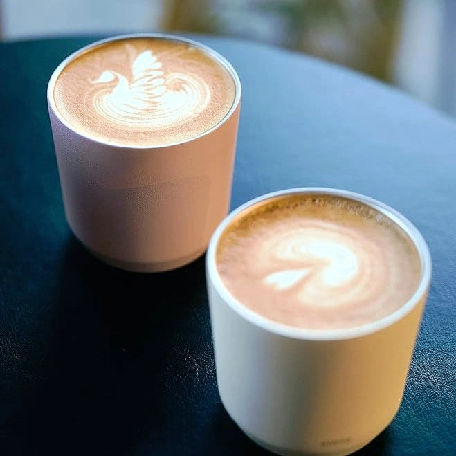 Dwa kubki termiczne Kinto To Go Tumbler z kawą mleczną i wzorami latte art