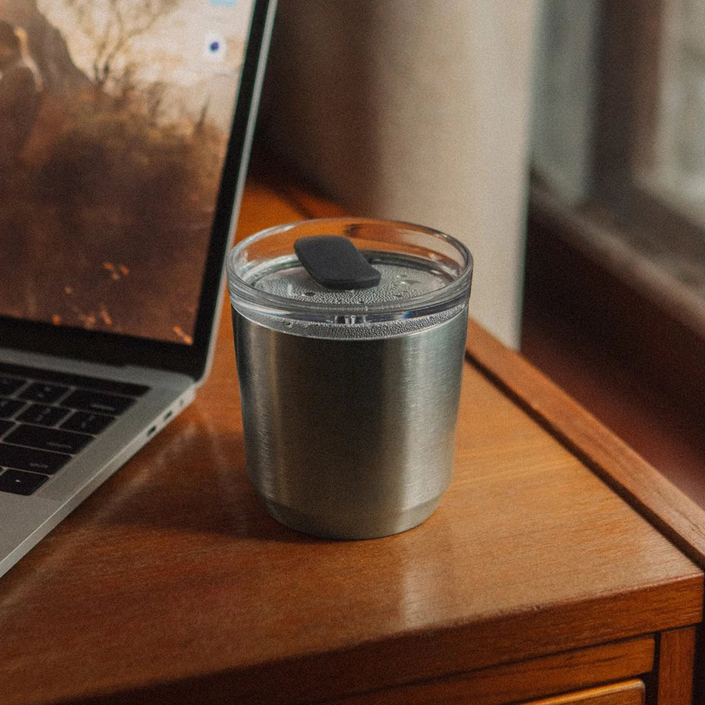 Srebrny kubek termiczny Kinto To Go Tumbler z pokrywką stojący obok laptopa