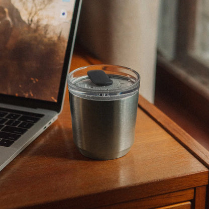 Srebrny kubek termiczny Kinto To Go Tumbler z pokrywką stojący obok laptopa