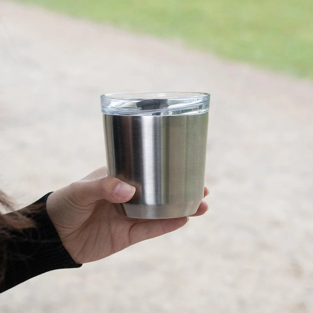 Srebrny kubek termiczny Kinto To Go Tumbler z przezroczystą pokrywką trzymany w dłoni