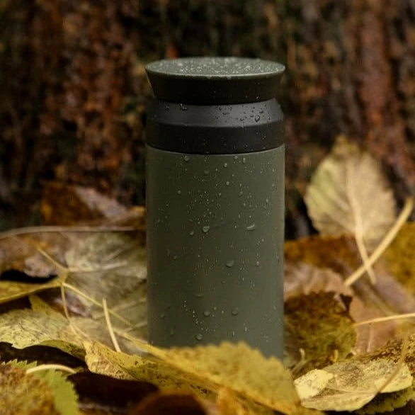 Zielony kubek termiczny Kinto Travel Tumbler wśród mokrych jesiennych liści w lesie
