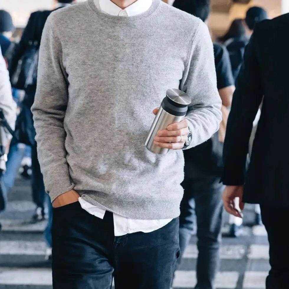 Mężczyzna w szarym swetrze trzyma kubek termiczny Kinto Travel Tumbler 350 ml w kolorze stalowym, ujęcie lifestyle w miejskim otoczeniu