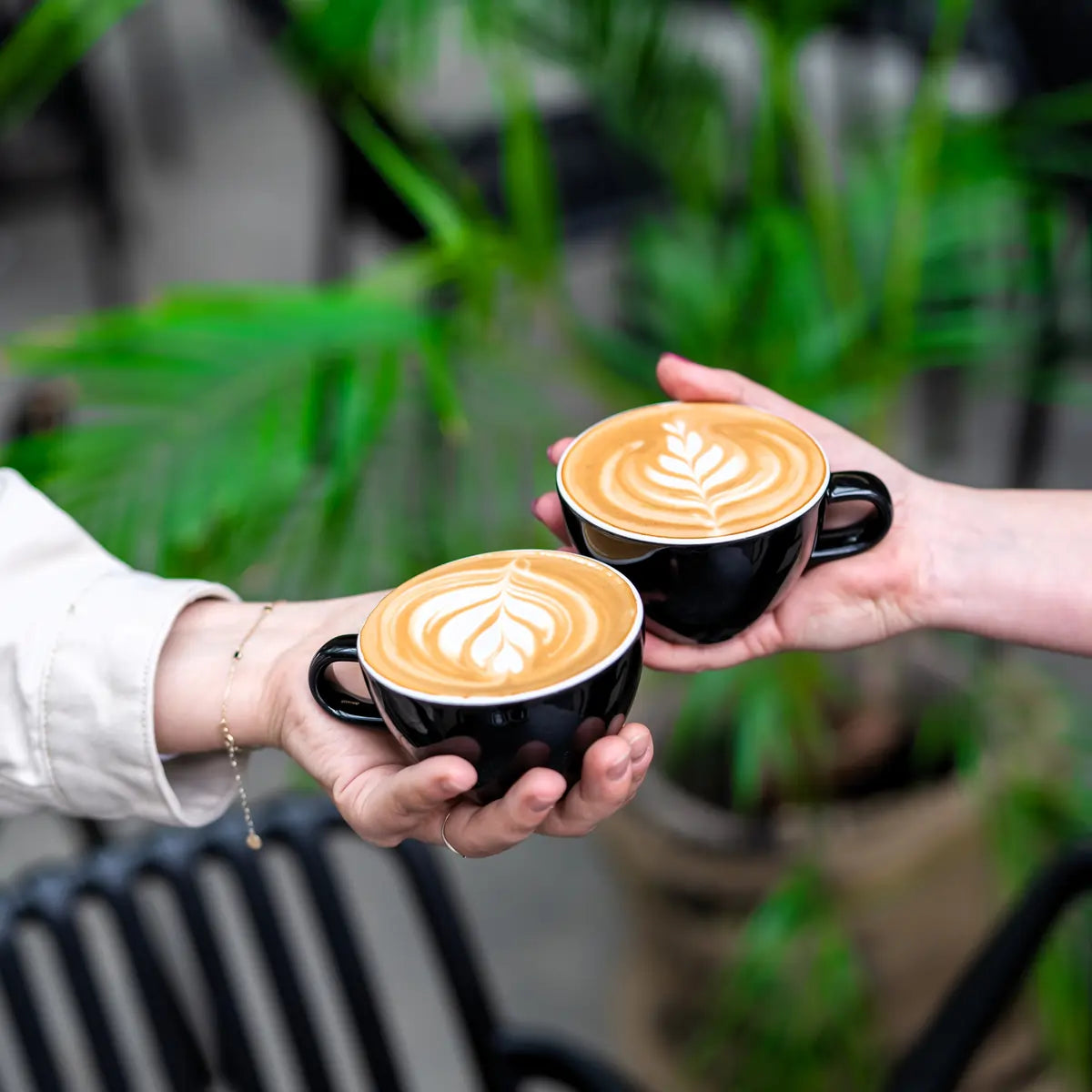 Dwie filiżanki kawy z latte art trzymane w dłoniach – efekt szkolenia Latte Art w JAVA Coffee