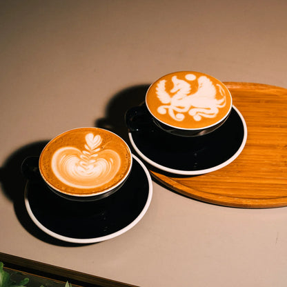 Dwie filiżanki cappuccino z latte art – wzory rozety i gryfa wykonane na aksamitnej mikropiance przez baristę.