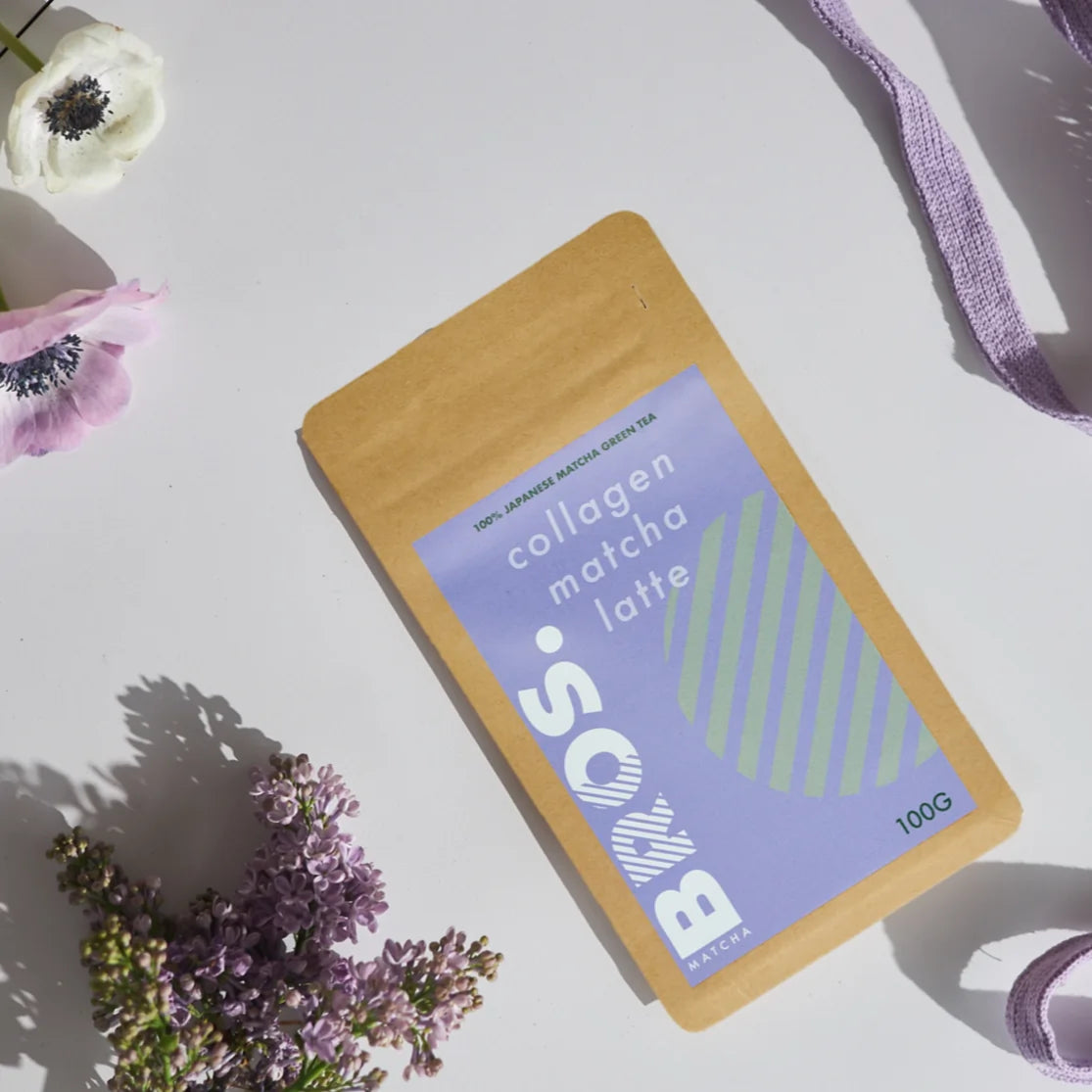 Matcha Bros Collagen Matcha Latte 100g – japońska matcha z kolagenem w opakowaniu kraft, zdjęcie lifestyle z kwiatami