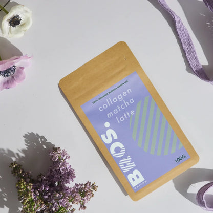 Matcha Bros Collagen Matcha Latte 100g – japońska matcha z kolagenem w opakowaniu kraft, zdjęcie lifestyle z kwiatami