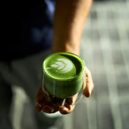 Matcha latte z latte art trzymana w dłoni, intensywnie zielona herbata matcha w szklance premium