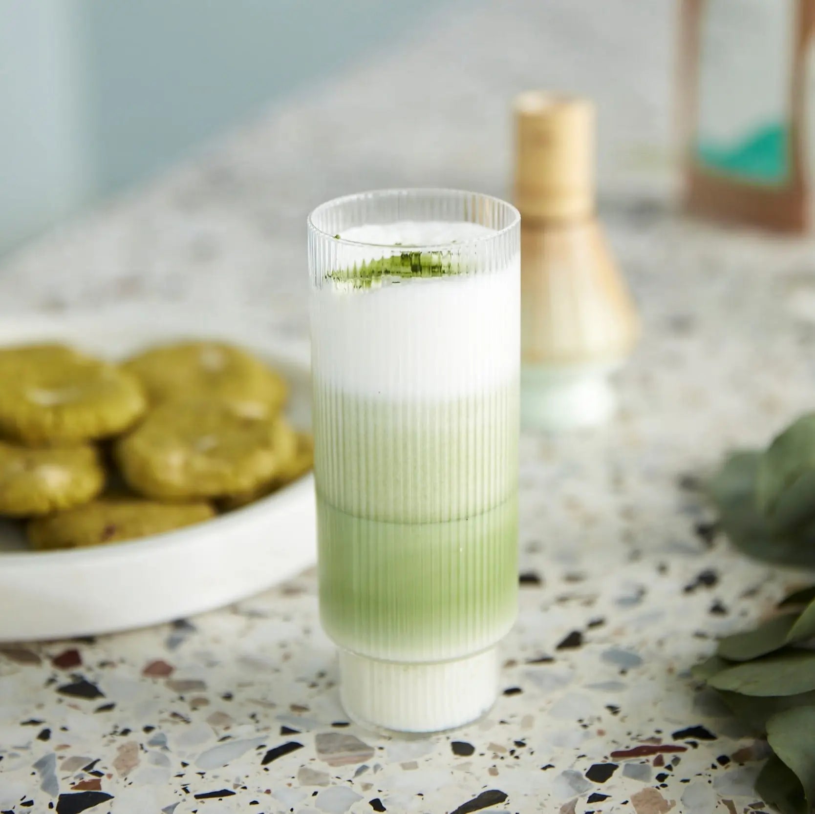 Warstwowe matcha latte z pianką mleczną w szklance na jasnym blacie, zielona herbata matcha Bros.