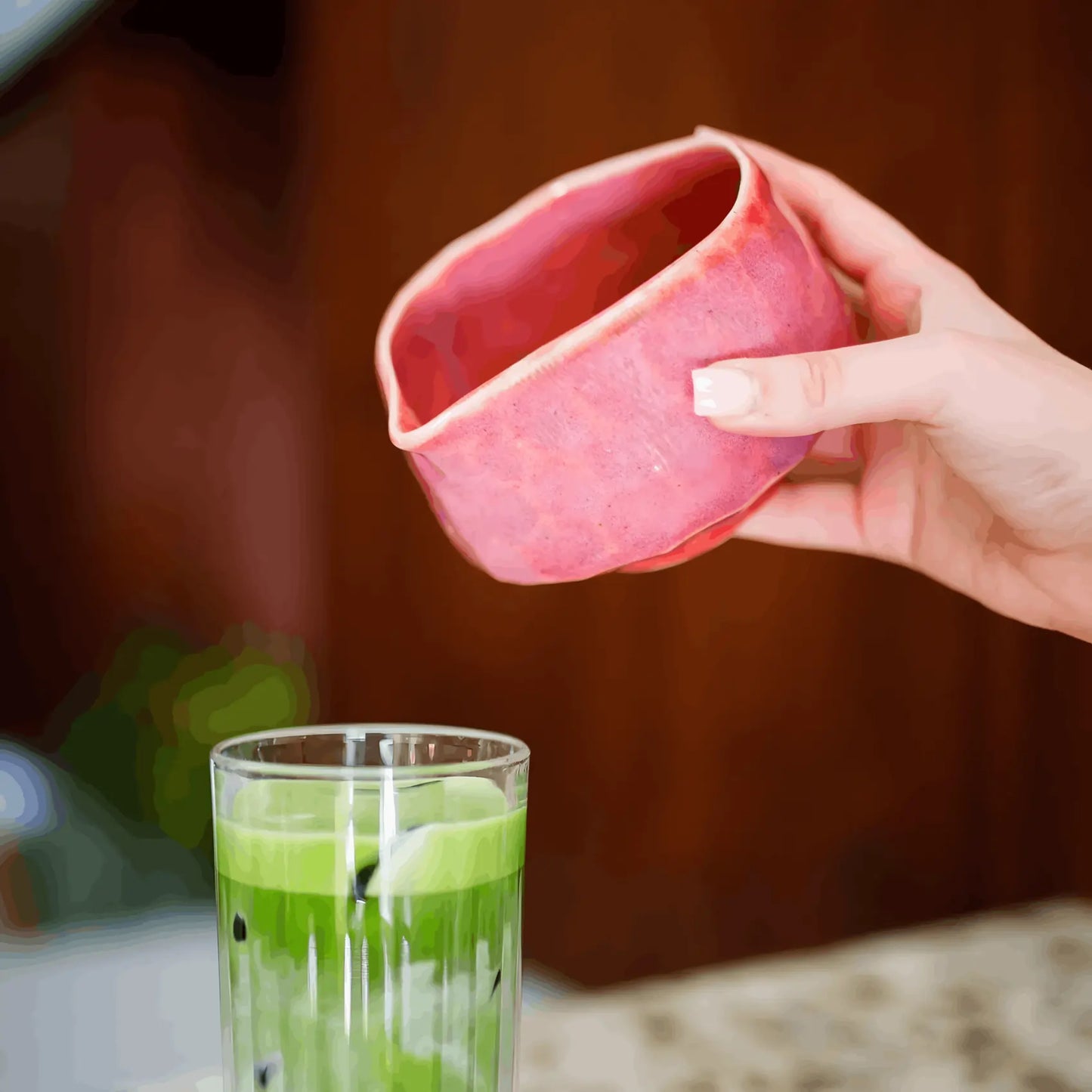 Różowa ceramiczna czarka do matchy z dziobkiem Matchawan Botan podczas nalewania matchy do szklanki z mlekiem i lodem.