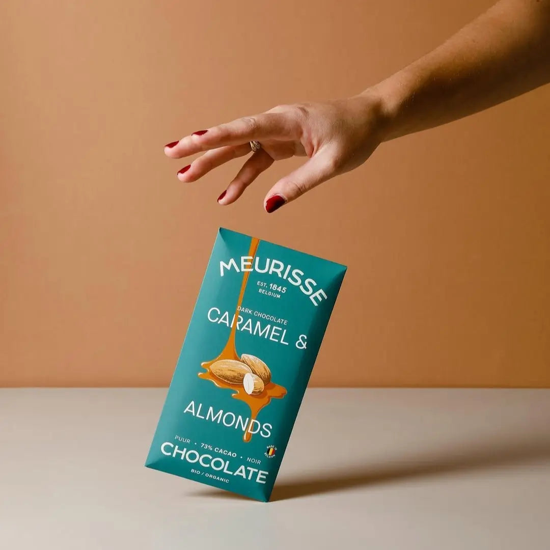 tabliczka czekolady Meurisse Caramel & Almonds trzymana w dłoni na beżowo-brązowym tle
