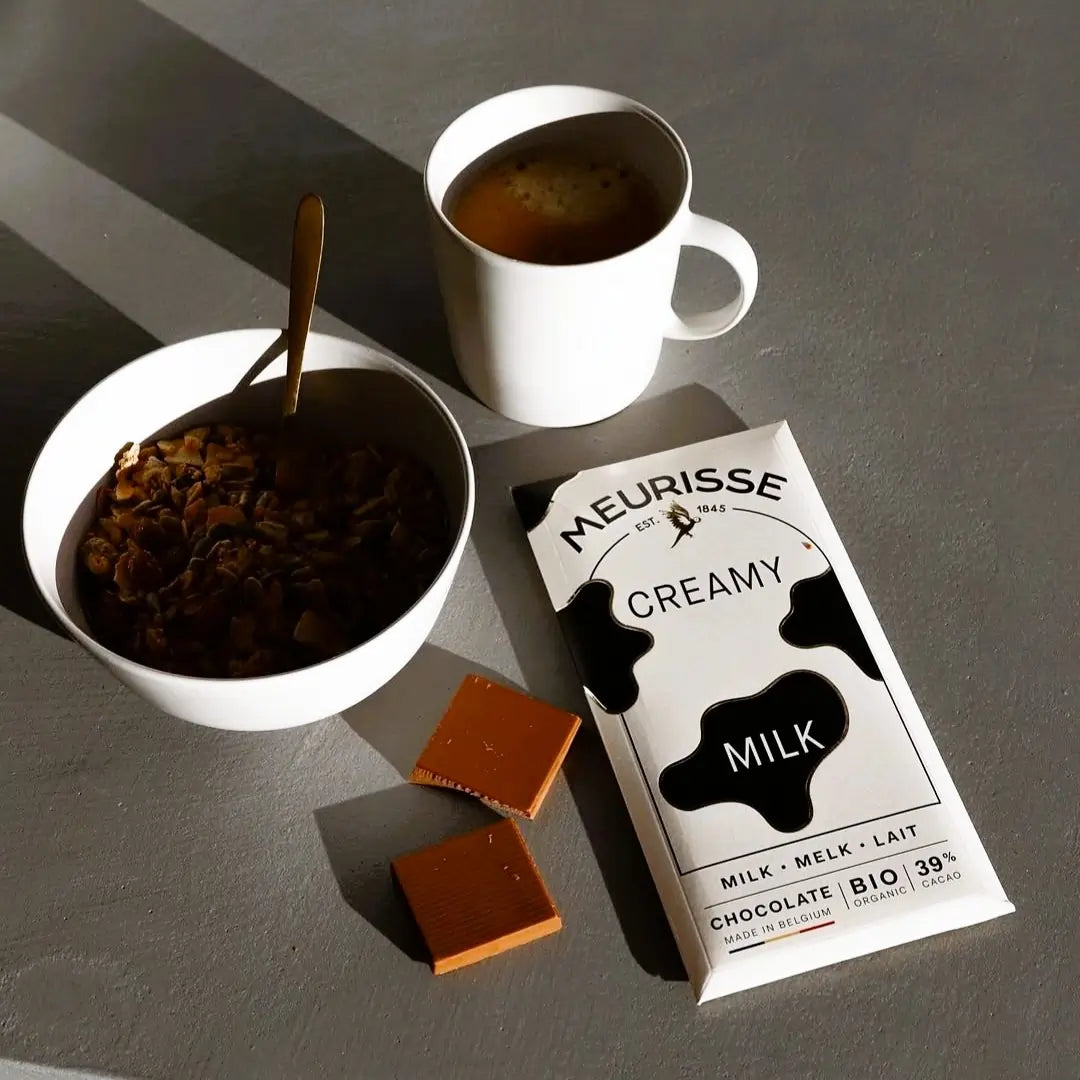 Tabliczka mlecznej czekolady Meurisse Creamy Milk 39% kakao obok filiżanki kawy i miski z granolą, w naturalnym świetle poranka.