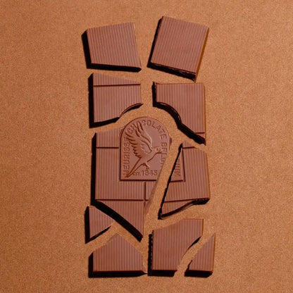 Połamane kawałki mlecznej czekolady Meurisse Creamy Milk z logo marki w centrum, na beżowym tle.