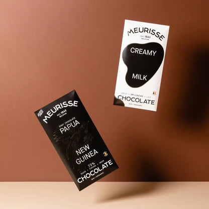 opakowania czekolad Meurisse Papua New Guinea 73% i Creamy Milk unoszące się nad brązowym tłem