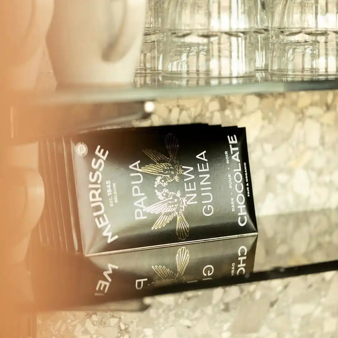 tabliczki czekolady Meurisse Papua New Guinea ułożone na półce obok filiżanek i szklanek