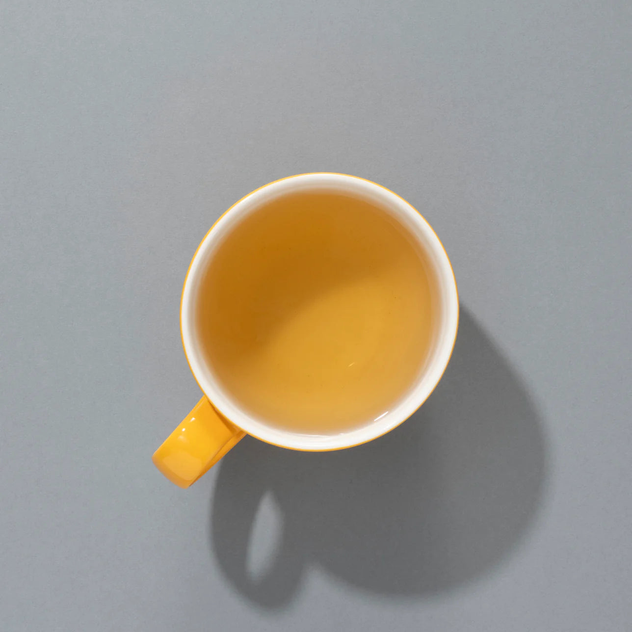 Napar herbaty owocowej Partridge in a Pear Tea SUKI Tea – widok z góry na filiżankę z jasnozłotym naparem w żółtym kubku na szarym tle.