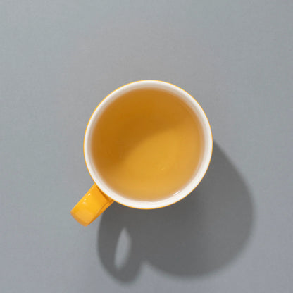 Napar herbaty owocowej Partridge in a Pear Tea SUKI Tea – widok z góry na filiżankę z jasnozłotym naparem w żółtym kubku na szarym tle.