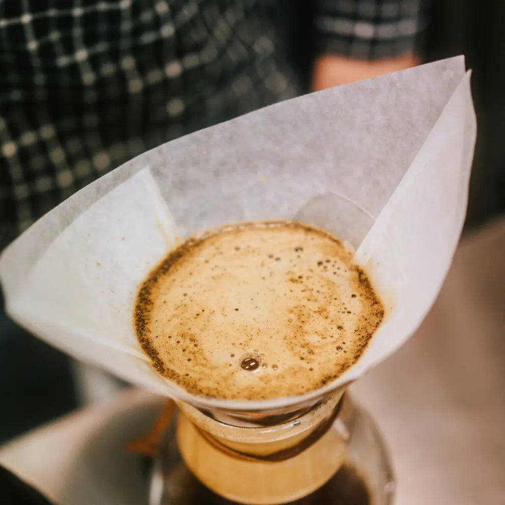 Zbliżenie na etap bloom podczas parzenia kawy w Chemexie z papierowym filtrem.