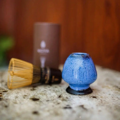 Niebieska ceramiczna podstawka do miotełki do matchy (chanoy) ustawiona na blacie obok bambusowej trzepaczki chasen, akcesoria do przygotowania matchy.